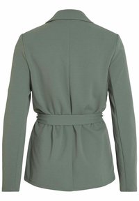 Grå långärmad kavaj med bälte i midjan, slagkrage och slät, strukturerad tyg. Bakifrån syns skräddarsydda sömmar och detaljer.