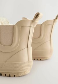 Beige gummistøvler til anklen med en tekstureret sål, afrundet bagdel og en blød stofforing. Har formede detaljer og en glat overflade.