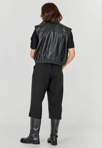 Nő háttal állva, fekete rövid ujjú felsőt, fekete bőrdzsekit, felvágott fekete nadrágot és térd fölé érő fekete csizmát visel.