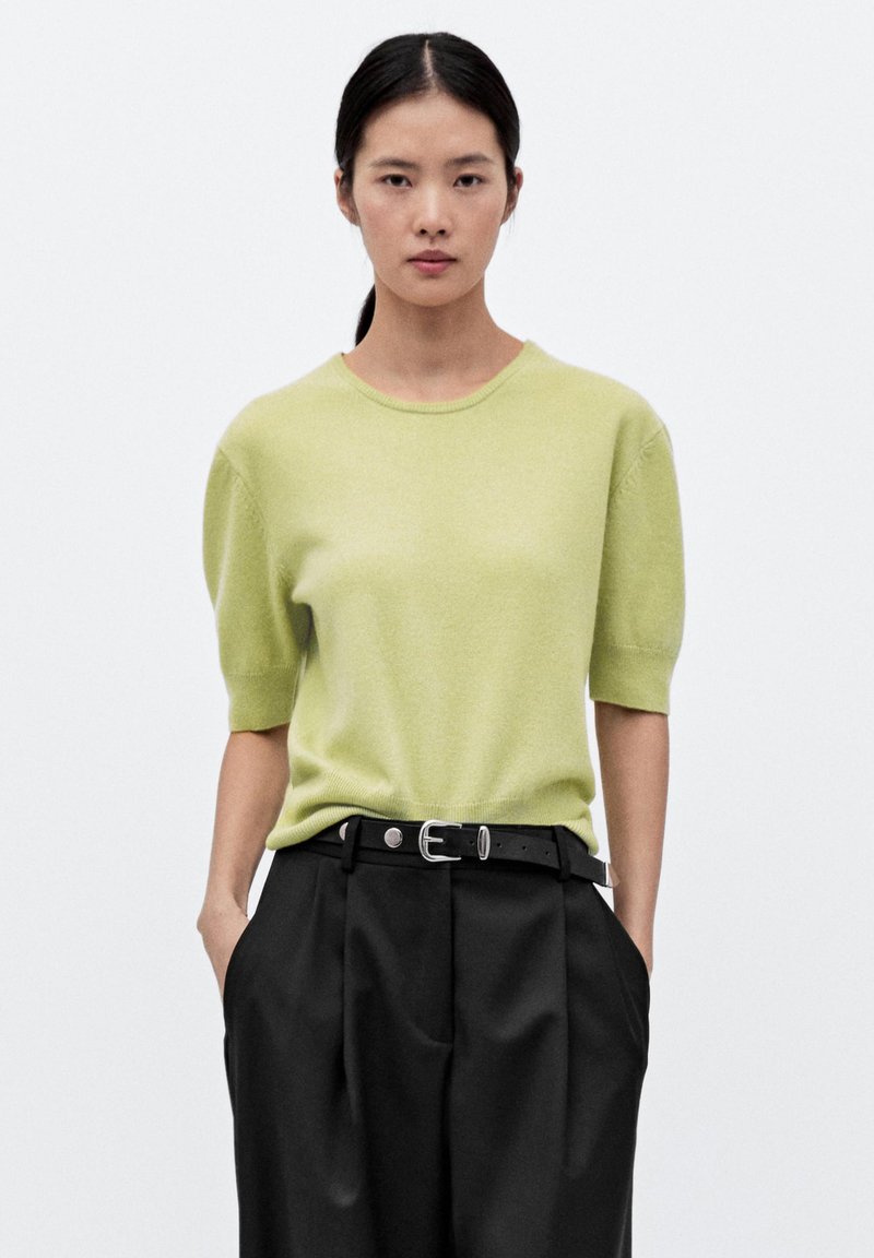 Maglione a maniche corte, di un verde chiaro in tessuto morbido, scollatura rotonda, abbinato a pantaloni neri a vita alta, larghi e con una cintura nera.