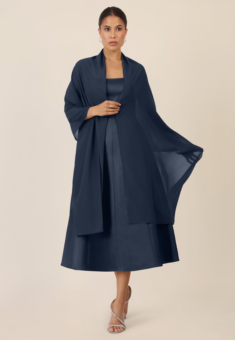 Abito a strati blu navy con corpetto in satin, sovrapposizione trasparente fluida e maniche larghe. Completato da sandali alti argentati con cinturini.