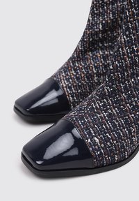 Botas de tobillo de punto en navy con motas multicolores, que presentan un cap toe de charol navy brillante y una parte superior de tela texturizada.