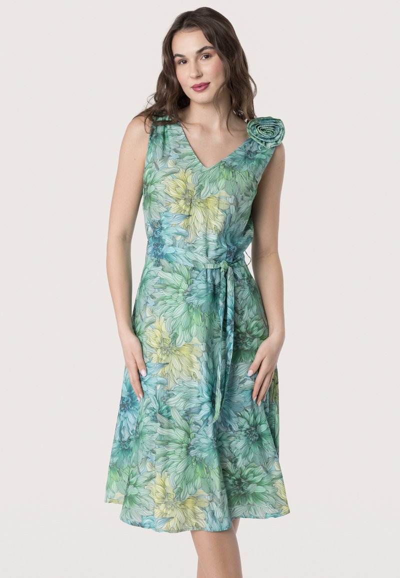 Bloemenjurk in blauwe, groene en gele tinten. Het V-hals ontwerp heeft een rozenaccent op één schouder en een riem in de taille.