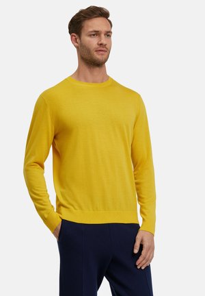 Maglione giallo a maglia con maniche lunghe, scollo rotondo e una texture morbida. Indossato con pantaloni blu scuro, dal design aderente e orlo a coste.