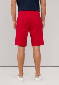 Rode shorts gemaakt van lichtgewicht stof, met een rechte snit en omgerolde mouwen. Heeft twee achterzakken met knoopsluiting en ceintuurlussen.
