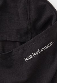 Melnas audums ar gludu tekstūru, ar redzamu balto logotipu "PeakPerformance". Kārtīgi šūtas malas.