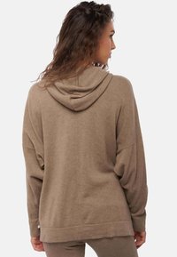 Sweat à capuche marron surdimensionné avec capuche et épaules tombantes, fabriqué en tissu doux. Il présente un ourlet droit et des détails de couture discrets.