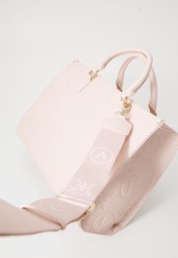Sac à main en cuir rose avec des motifs floraux embossés, quincaillerie dorée, double poignées supérieures et bandoulière en tissu amovible.