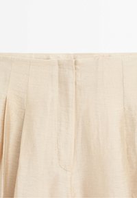Tissu beige plissé avec coutures verticales, probablement partie de la ceinture et de la zone de fermeture avant d'un vêtement.