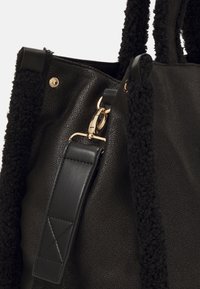 Sac à main noir texturé avec bordure en polaire douce, fermoir doré et bandoulière en cuir amovible en gros plan.