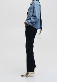 Giacca di jeans blu chiaro, pantaloni neri e scarpe con tacco alto metalliche dorate. Le caratteristiche includono un design strutturato e un taglio dritto.