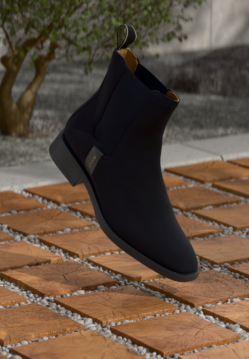 Stivale Chelsea in pelle nera con texture liscia, fodera interna gialla e suola nera, dotato di un anello per facilitare l'indossamento.