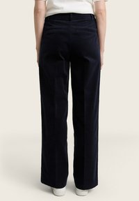 Pantaloni in corda a gamba larga di colore navy con vita alta, dotati di due tasche posteriori e una sottile texture a coste, abbinati a sneakers bianche.