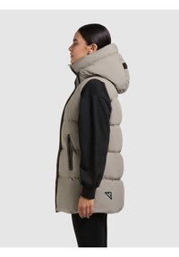 Kergelt hall säär, millel on kõrge kaelus, lukuga taskud ja mustad aktsendid. Mudel kannab all musta pika varrukaga särke.