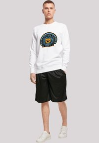 Hvid sweatshirt med "City of Gotham Police Department" emblem, parret med sorte shorts og hvide sneakers. Uformelt atletisk tøj.