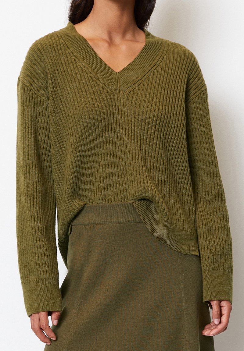 Maglione a coste verde oliva con scollatura a V e maniche lunghe. Il tessuto appare testurizzato, abbinato a una gonna coordinata.