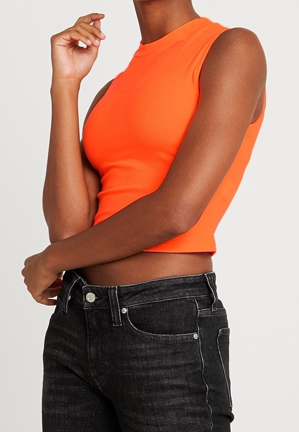 Haut court ajusté sans manches de couleur orange vif porté avec un jean noir taille haute sur une personne à la peau de teint moyen-foncé.