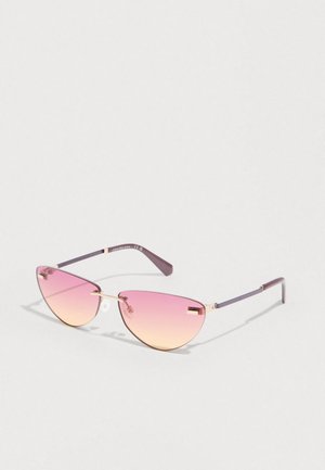 Óculos de sol em formato de olhos de gato, em roxo e dourado, com lentes em degradê do rosa ao laranja e hastes finas de metal, sobre um fundo claro.