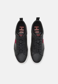 Baskets basses noires avec lacets noirs, semelles blanches et logo rouge "HUGO" sur la languette et les côtés, vues de dessus.