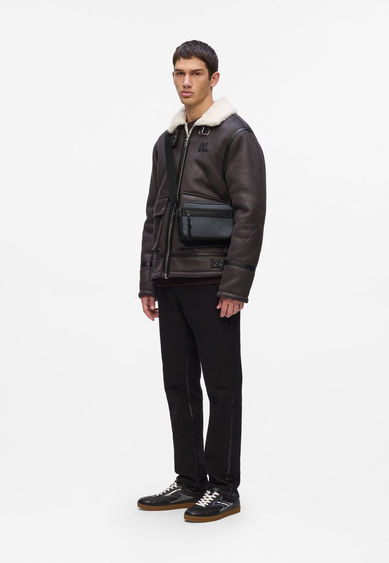Giubbotto di pelle marrone con collo in pelliccia, pantaloni neri aderenti e sneakers nere con dettagli bianchi; borsa a tracolla in pelle nera.