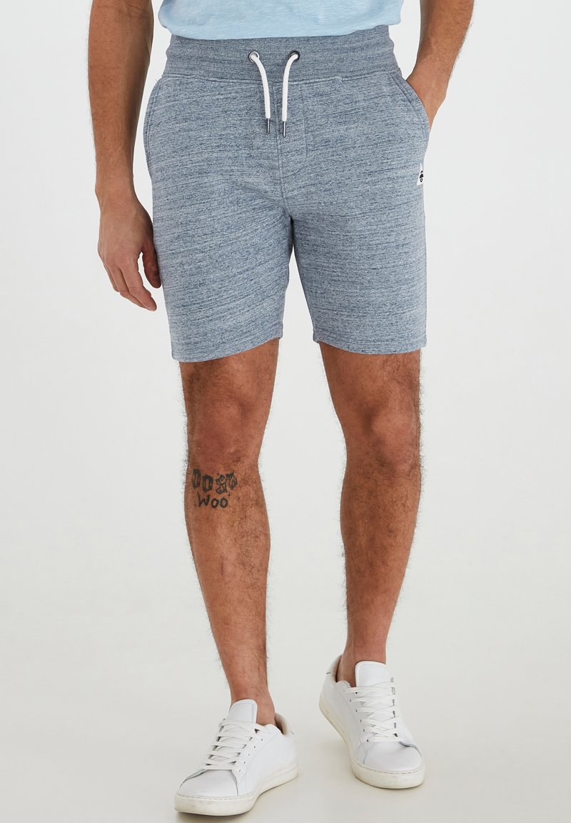 Pantalones cortos de sudadera en gris melange con cintura elástica y cordón. Cuenta con bolsillos laterales y un corte ajustado. Combinados con zapatillas blancas.