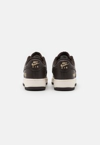 Un par de zapatillas Nike Air de color marrón oscuro vistas desde atrás, con mediasoles beige y suelas negras sobre un fondo blanco.