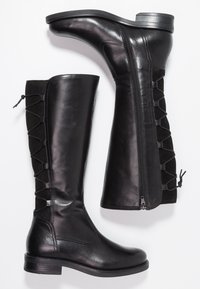 Botas negras hasta la rodilla con parte superior de cuero suave, panel lateral de gamuza negra texturizada con cordones, y tacón bajo. Cremallera en un lado.
