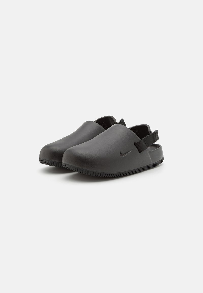 Zwarte synthetische klompen met een ronde neus, open achterkant en een gestructureerde zool. Voorzien van een klein Nike-logo en een verstelbare band op de hiel.