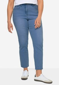 Vaqueros de tiro alto en denim azul medio, corte recto, diseño de cinco bolsillos, estilizados con zapatillas blancas y una camiseta blanca básica.