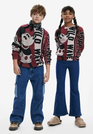 Zwei Kinder tragen gestrickte Pullover mit auffälligen Mickey-Mouse-Grafiken in Rot und Schwarz, kombiniert mit blauen Schlagjeans und bequemen Schuhen.