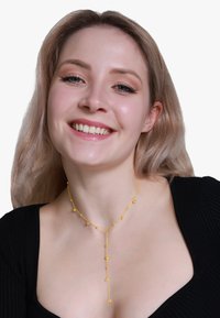 Collana in oro con pendenti circolari, link delicati e un design a forma di Y, poggiata su un top nero. Texture liscia, finitura lucida.