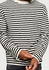 Sweter w paski w kolorze białym i czarnym, z okrągłym dekoltem, długimi rękawami, teksturowaną tkaniną oraz widocznymi drobnymi detalami postarzania.