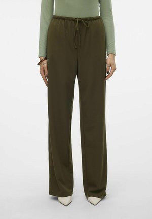 Pantalons larges en vert olive avec une taille élastique et un cordon de serrage. Tissu doux avec une texture lisse ; associés à des chaussures à bout pointu crème.