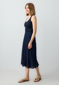 Top a righe color blu navy abbinato a una gonna fluida e plissettata blu navy. La gonna è dotata di una vita elastica e arriva a metà polpaccio.