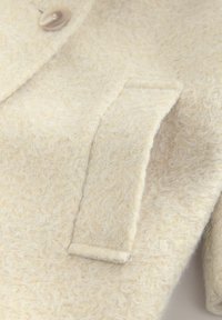 Elfenbeinfarbene Wollmischjacke mit einem weichen, strukturierten Stoff, einem einzelnen Knopf und einer Klappentasche auf der linken Seite.