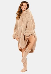 Hoodie oversize beige realizzato in materiale morbido e soffice. Presenta maniche lunghe, cappuccio, una tasca frontale e scaldamuscoli abbinati in pelouche.