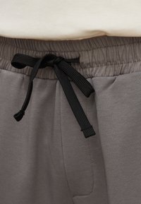Graue Jogginghosen mit einem elastischen Bund und schwarzem Kordelzug, glatter Textur und seitlichen Taschen.