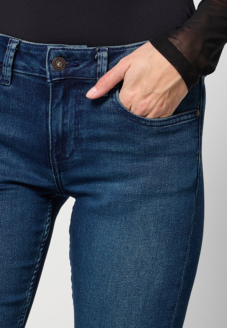 Jeans in denim blu scuro con un design aderente, cinque tasche, chiusura con bottone e una leggera texture di sfumatura nella parte anteriore.
