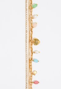 Pulsera de oro con piedras preciosas coloridas: acentos en verde, rosa, azul y rojo, con un pequeño charm en forma de corazón y cristales brillantes.