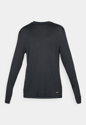 Sort langærmet træningsskjorte lavet af struktureret stof. Har en rund halsudskæring og et diskret Nike-logo i lyseblå nederst til højre.
