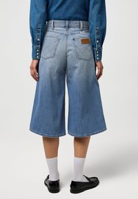 Ljust blå denimculotter har hög midja, vida ben och bakfickor. Anmärkningsvärda detaljer inkluderar en brun läderetikett och stickade fållar.