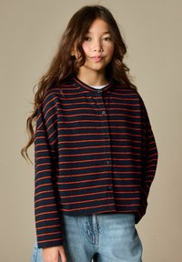 Donkerblauw en rood gestreept overhemd met lange mouwen en knopen, met een ronde halslijn, gedragen over een wit shirt en gecombineerd met lichtblauwe denim.