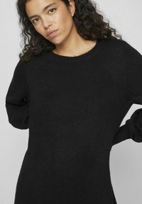 Maglione nero lavorato a maglia con collo rotondo e maniche lunghe. Il tessuto appare morbido e strutturato, e la silhouette è rilassata e leggermente oversized.