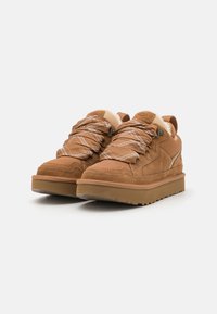 Bruine suède sneakers met textuuraccenten, gewatteerde kraag en dikke rubberen zolen. Kenmerken zijn patroonveters en logo-detailing op de tong.