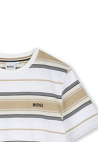 Maglietta a righe in bianco, beige e nero. Presenta un collo rotondo, maniche corte e un piccolo logo stampato "BOSS" vicino al petto.
