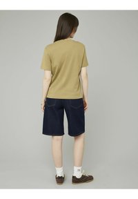 T-shirt kaki à manches courtes associé à un short en denim bleu foncé, avec des coutures visibles et des poches arrière ; porté avec des chaussettes blanches et des chaussures marron.