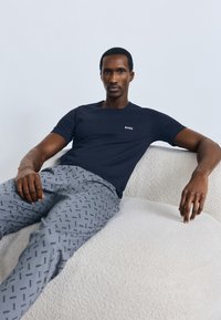 Maglietta a maniche corte in cotone blu navy con logo "BOSS", abbinata a pantaloni grigio chiaro con motivo a logo ripetuto. Design semplice e moderno.