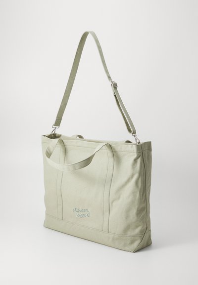 Bolsa tote de lona verde claro con dos asas superiores, correa ajustable y detalle bordado "maison" en el frente, que presenta una forma estructurada.