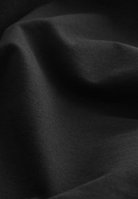La tela negra presenta una textura suave y mate con sutiles arrugas y pliegues, destacando su calidad blanda y elástica y su color uniforme.