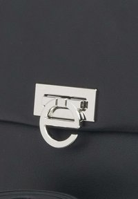 Zwarte leren handtas met een rechthoekige zilveren sluiting en een cirkelvormige accent. Glad materiaal met minimalistische ontwerpelementen.